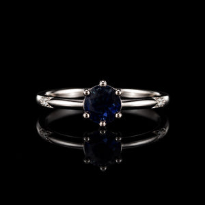 Aura Midnight Sapphire Ring featuring a deep-blue round crystal solitaire set on a polished silver-tone band with sparkling accent stones.