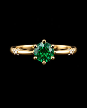 Aura Emerald Royale Ring featuring a brilliant emerald-green round crystal in a gold-tone solitaire setting with sparkling accent stones.